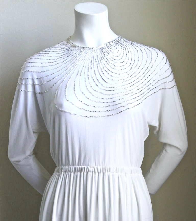 White silk jersey dress with silver bugle beads from Halston dating to the 1970's. Fits a size 2 or 4. The fit is narrow lower arms/wrists. Snap closure at wrists and hook/eye at back of neck. Approximate measurements: elastic waistband is 20