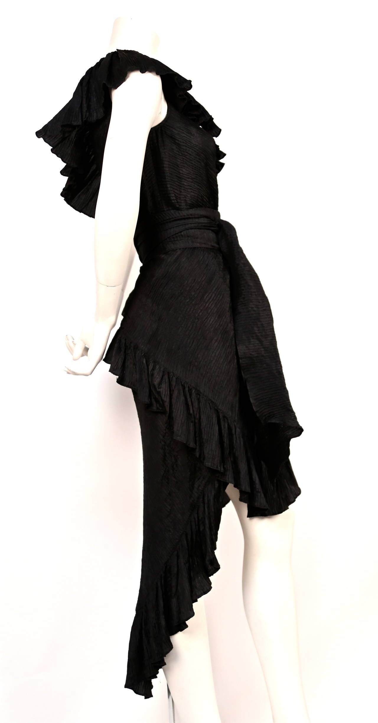 Jet black pleated silk dress with asymmetrical hemline from Yves Saint Laurent dating to the 1970's. Matching long sash included. Approximate measurements: bust 34
