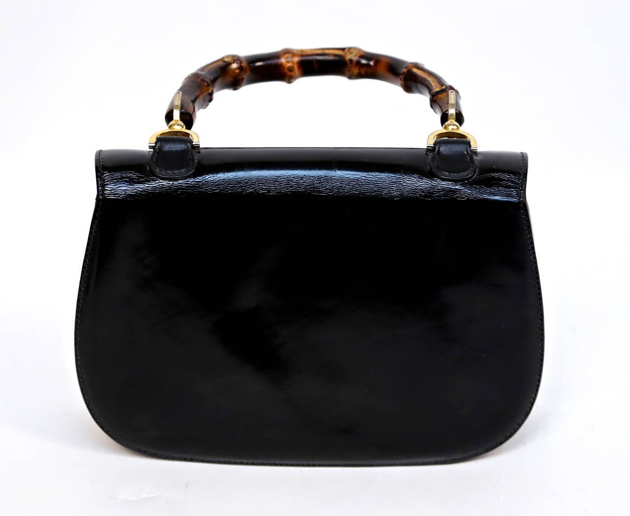 Jet black patent leather bag with brown bamboo and brass handle designed by Gucci dating to 1975. Bag measures approximately 10.5