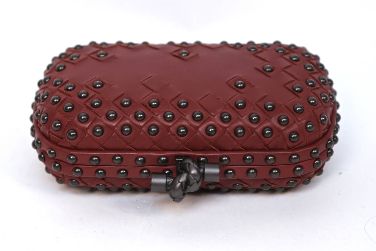 Burgundy intrecciato woven leather clutch bag with gunmetal studs and metal 'braided' snap-top clasp from Bottega Veneta. Approximate measurements: width 6.75