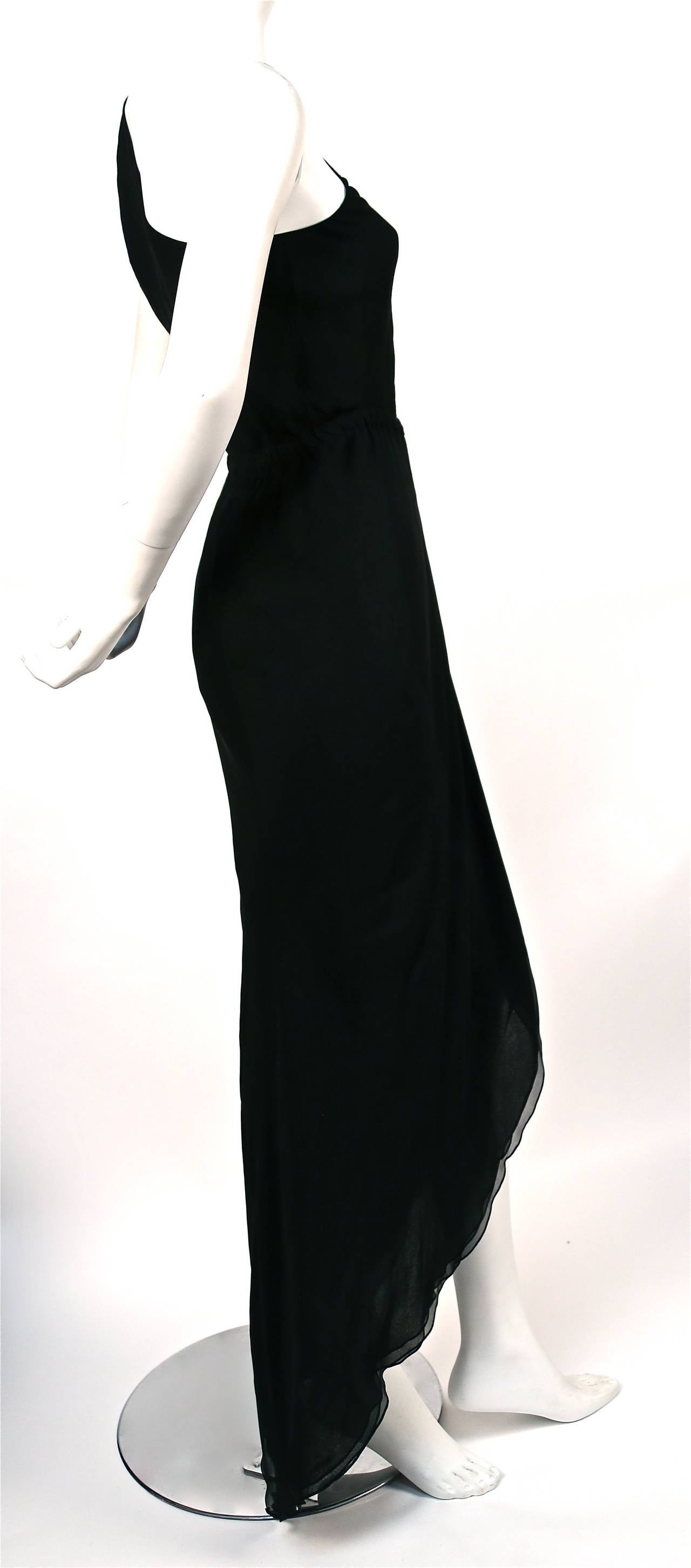 Jet black triple layer silk chiffon dress with asymmetrical shoulder, raised elasticized waistline and flounced hemline from hailstone dating to the 1970s. No size is indicated although this dress best fits a size 2 or more petite 4. Fabric is cut