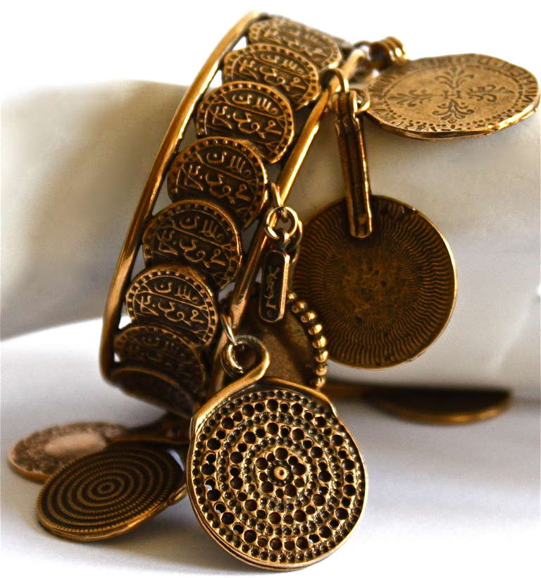 Very rare antiqued brass coin cuff with coin charms from Yves Saint Laurent dating to 1977. Cuff fits a small to medium sized wrist. Perimeter of cuff measures just under 8