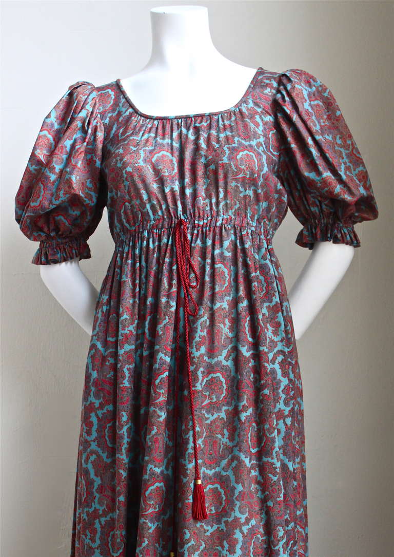 Very rare cotton floral paisley peasant gown with empire waist, contrasting side panels and sleeves, and a corded waist tie with tassels from Yves Saint Laurent dating to the 1970's. Labeled a French size 38. Approximate measurements: shoulders 14