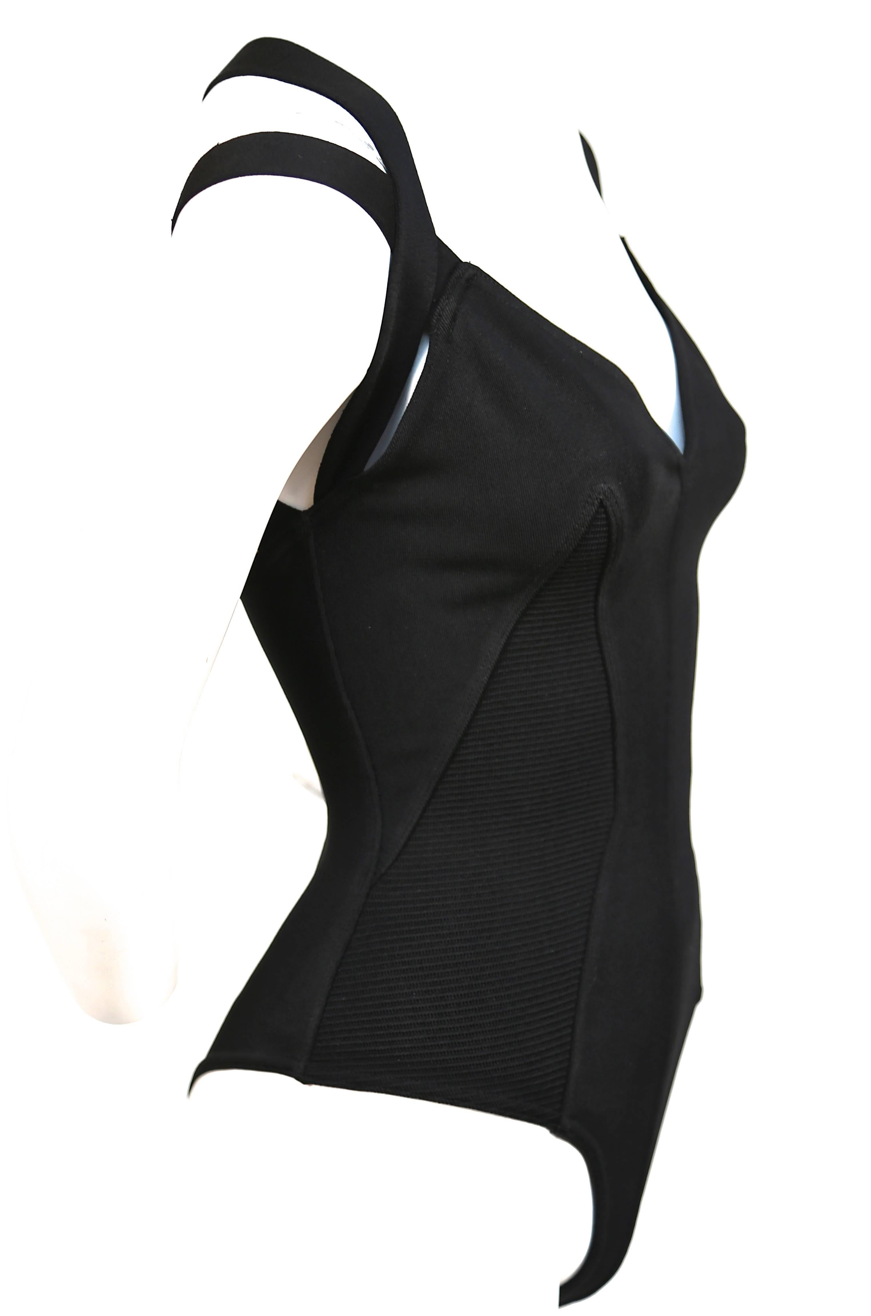 Jet black bodysuit with ribbed inserts and crossed shoulder straps from Azzedine Alaia dating to the 1990's. Labeled a size 'XS'. Best fits an XS or S. Made in Italy. Snap crotch closure. Excellent condition with one small repair at shoulder strap.