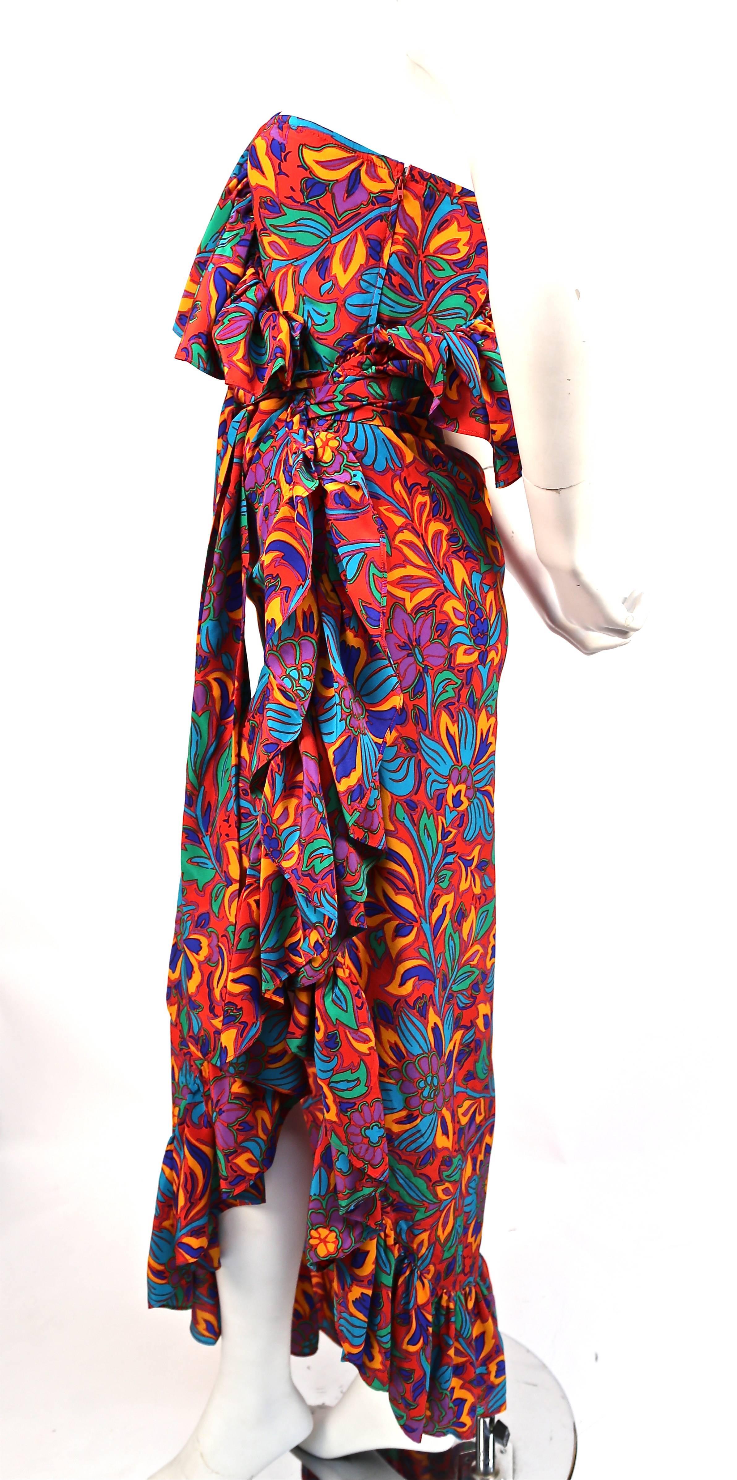 Vivid floral printed silk dress with asymmetrical shoulder and ruffled trim from Yves Saint Laurent dating to the 1970's. Self tie belt at waist. Dress is labeled a French size 34. Approximate measurements: bust unstretched is about 28