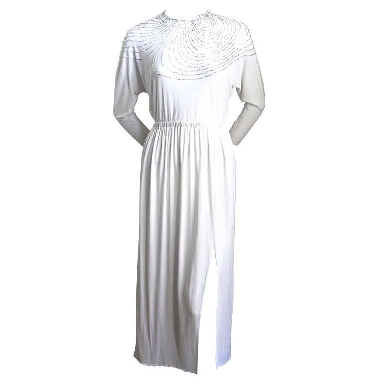 White silk jersey dress with silver bugle beads from Halston dating to the 1970's. Fits a size 2 (fits very narrow lower arms/wrists). Snap closure at wrists and hook/eye at back of neck. Approximate measurements:  elastic waistband is 20