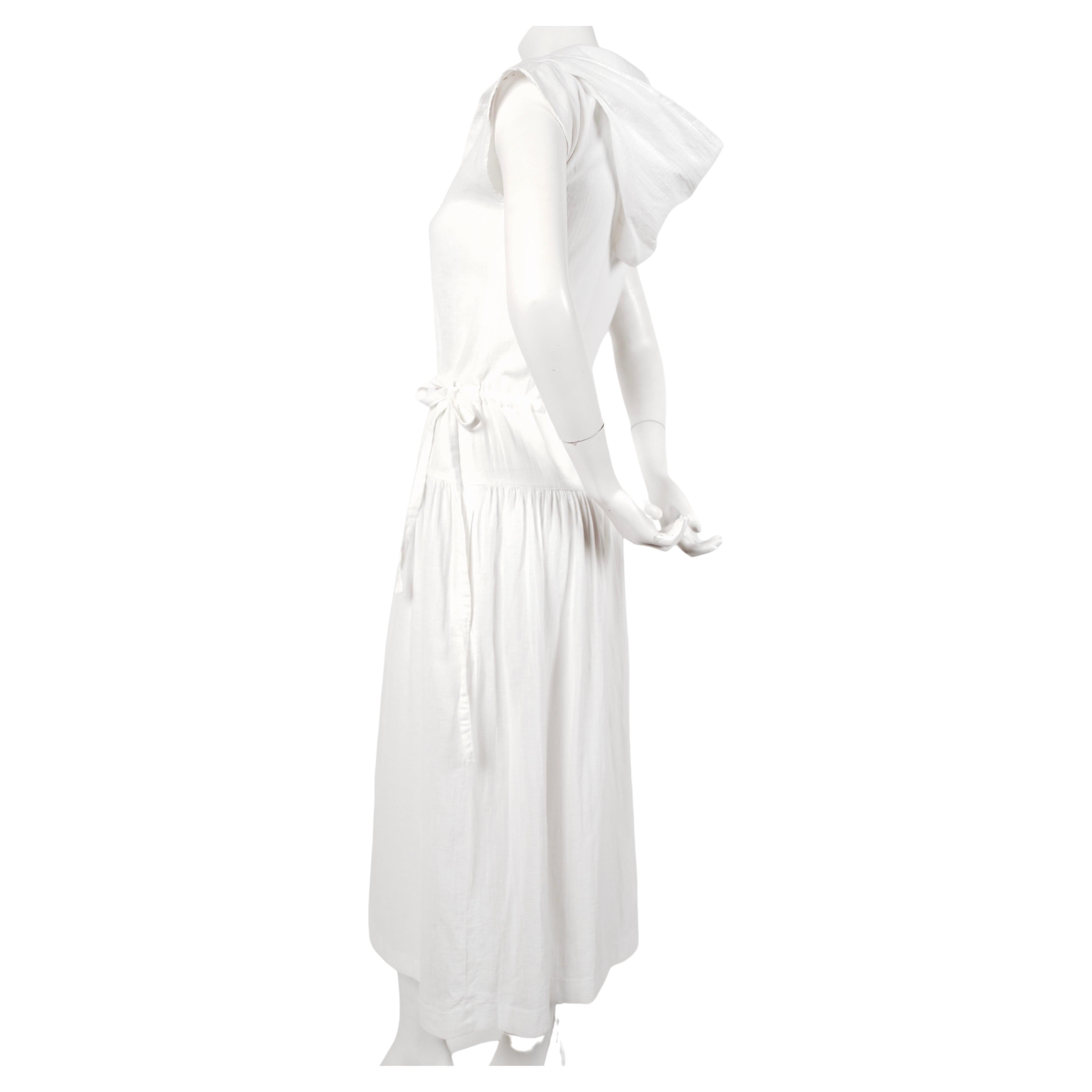 White gauze dress, with asymmetrical front pocket, drawstring waist, cap-sleeves and hood designed by Cacharel dating to the late 1970's. Labeled a FR 38 however this would best fit a FR 34-36 or US 2. Approximate measurements: Bust 31-32