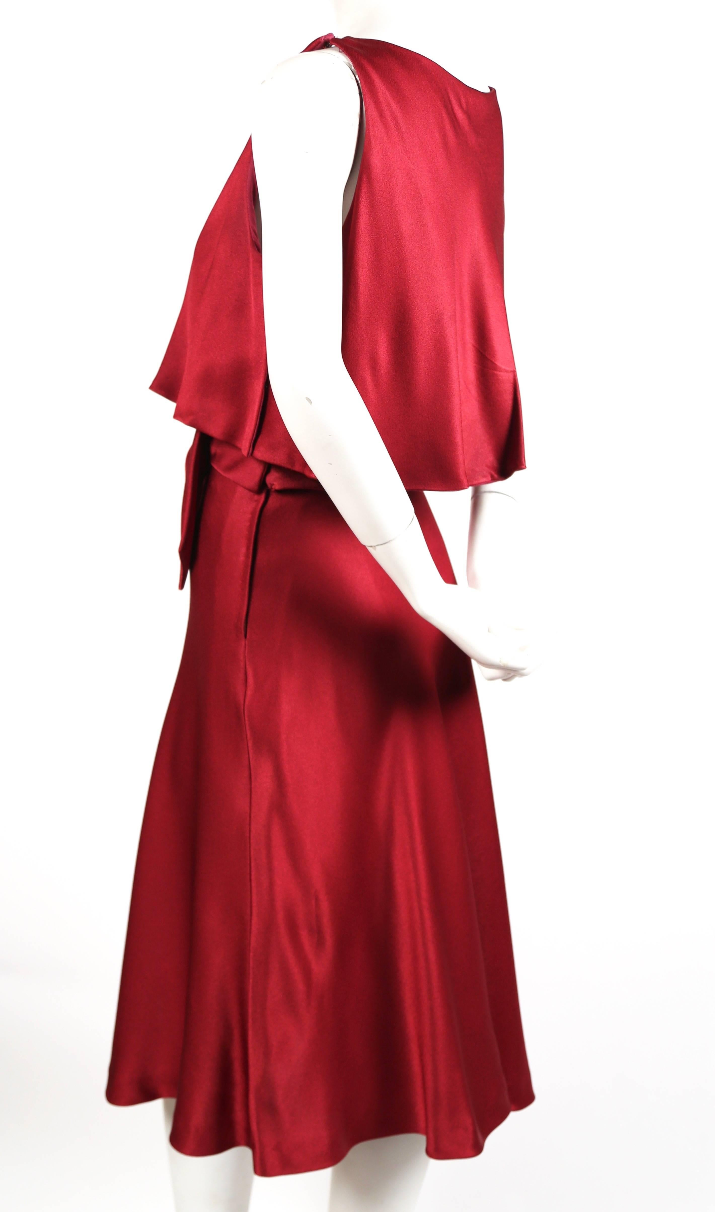 Vivid cranberry dress with crystal detail at waistline from Luis Estevez dating to the late 1960's. Top layer falls loosely over the bodice with a fitted under-layer and waistline. Bow detail with crystals. Dress best suited for a US 4 or 6.