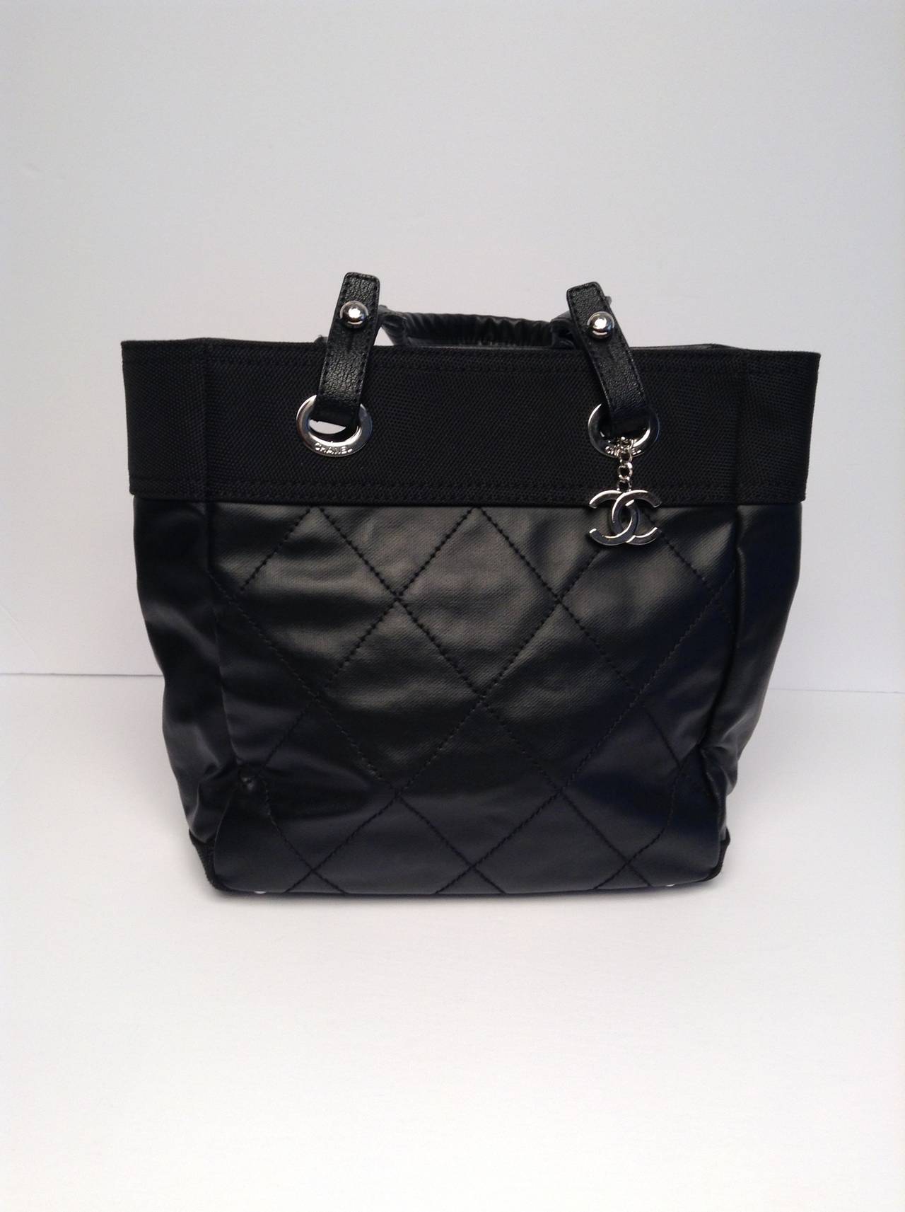This is an authentic CHANEL Coated Canvas Paris Biarritz Tote in Black. This super-chic tote is crafted of diamond stitched coated canvas. The bag features tall leather strap top handles with silver hardware including a hanging Chanel CC medallion,