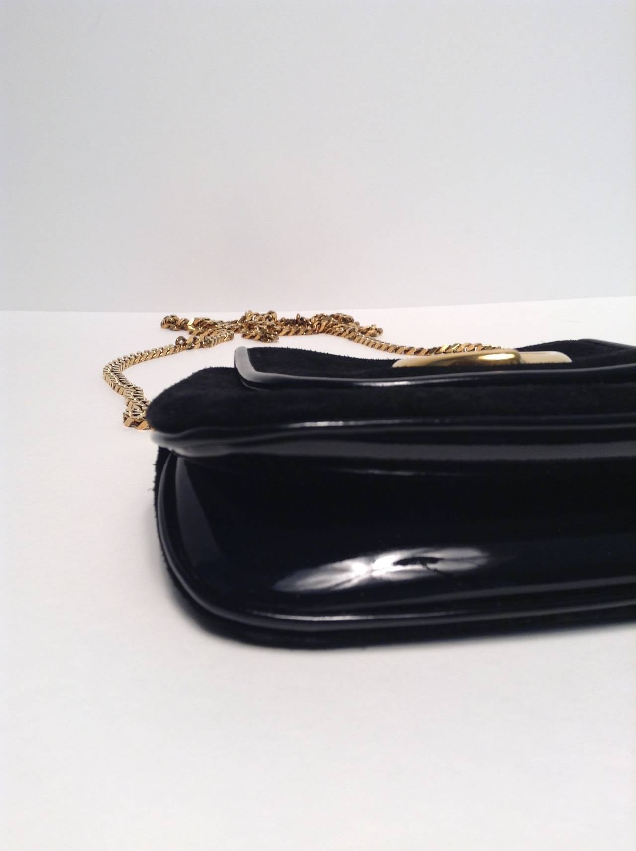 Finish off any evening ensemble with this classic Gucci Black Suede Gold Chain shoulder bag. The 1973 Reissue features black suede with a pop of black patent leather at the trim and bottom. Gold hardware and gold chain. Button flap closure. One wall
