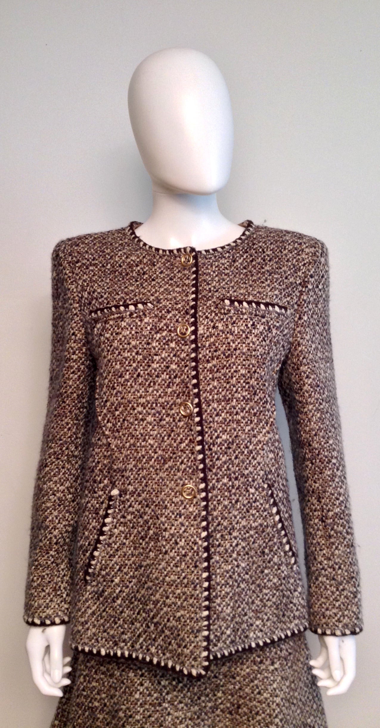 Classic Chanel tweed suit. Grey, brown, cream, and tan make up the tweed. 

Banded cuffs, pockets, and jacket edge. Jacket interior hem chain intact.

Lined with silk CC pattern. 

Measurements: bust 40