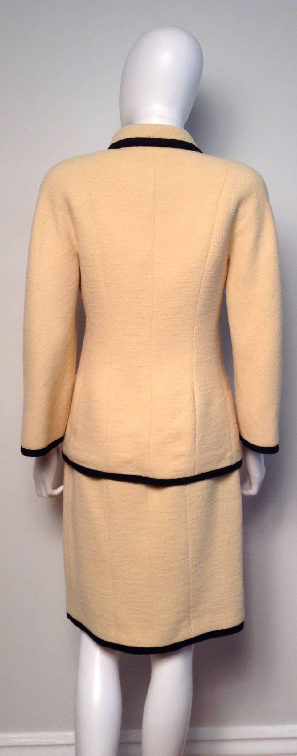 Bold black trim decorates cream tweed on this beautiful Chanel Skirt Suit from collection 25/1987. Features long sleeves, gold CC buttons and four flat front pockets. Fully lined. Button up closure. 

Measurements: Jacket: bust 35