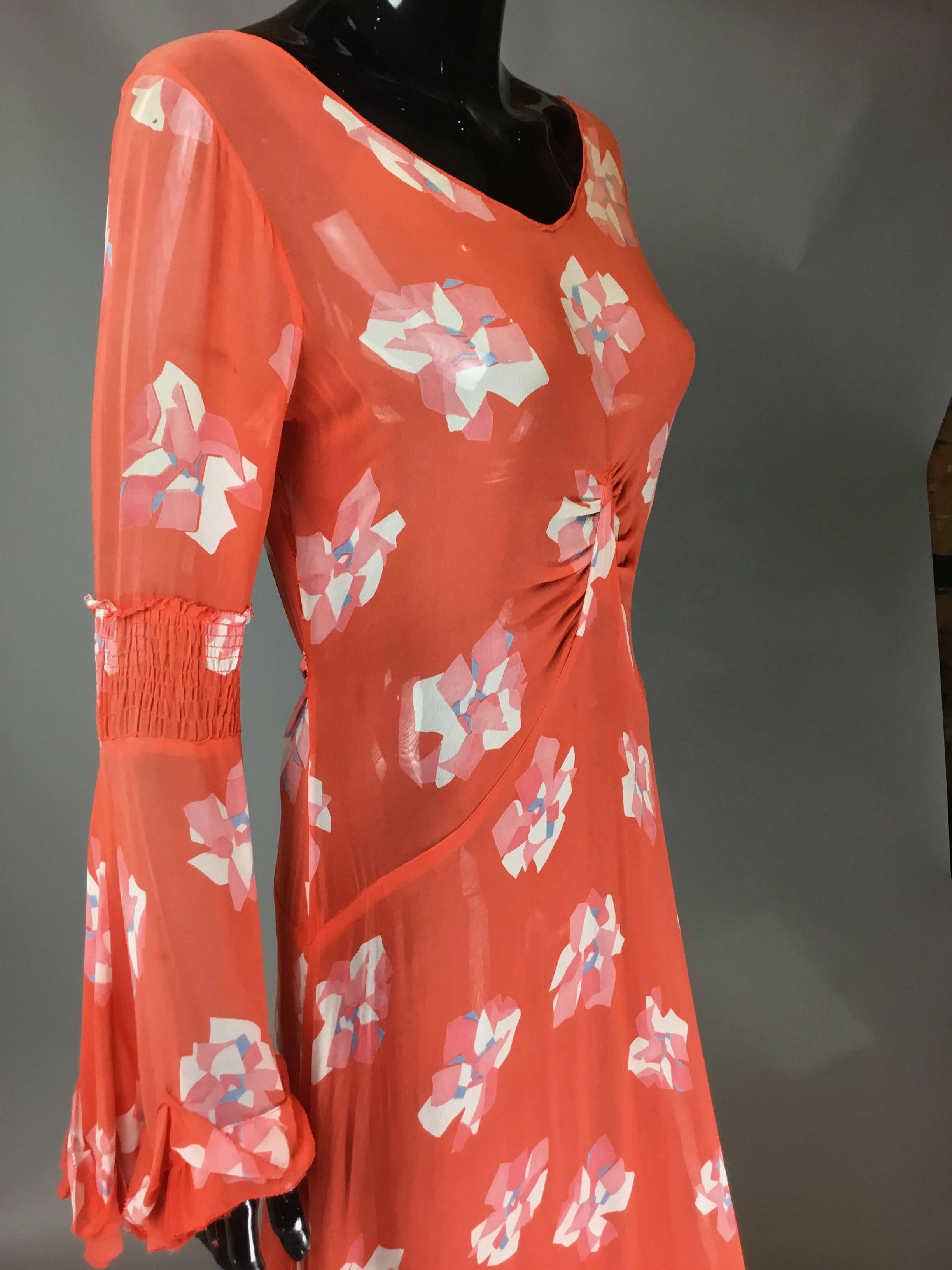 A beautiful 30s chiffon dress with a very deco style rose print. Gathering at central bust, and an attached self belt at rear, this dress falls down into a three tier ruffle hem. The sleeves have ruching halfway down that then fall into a wide