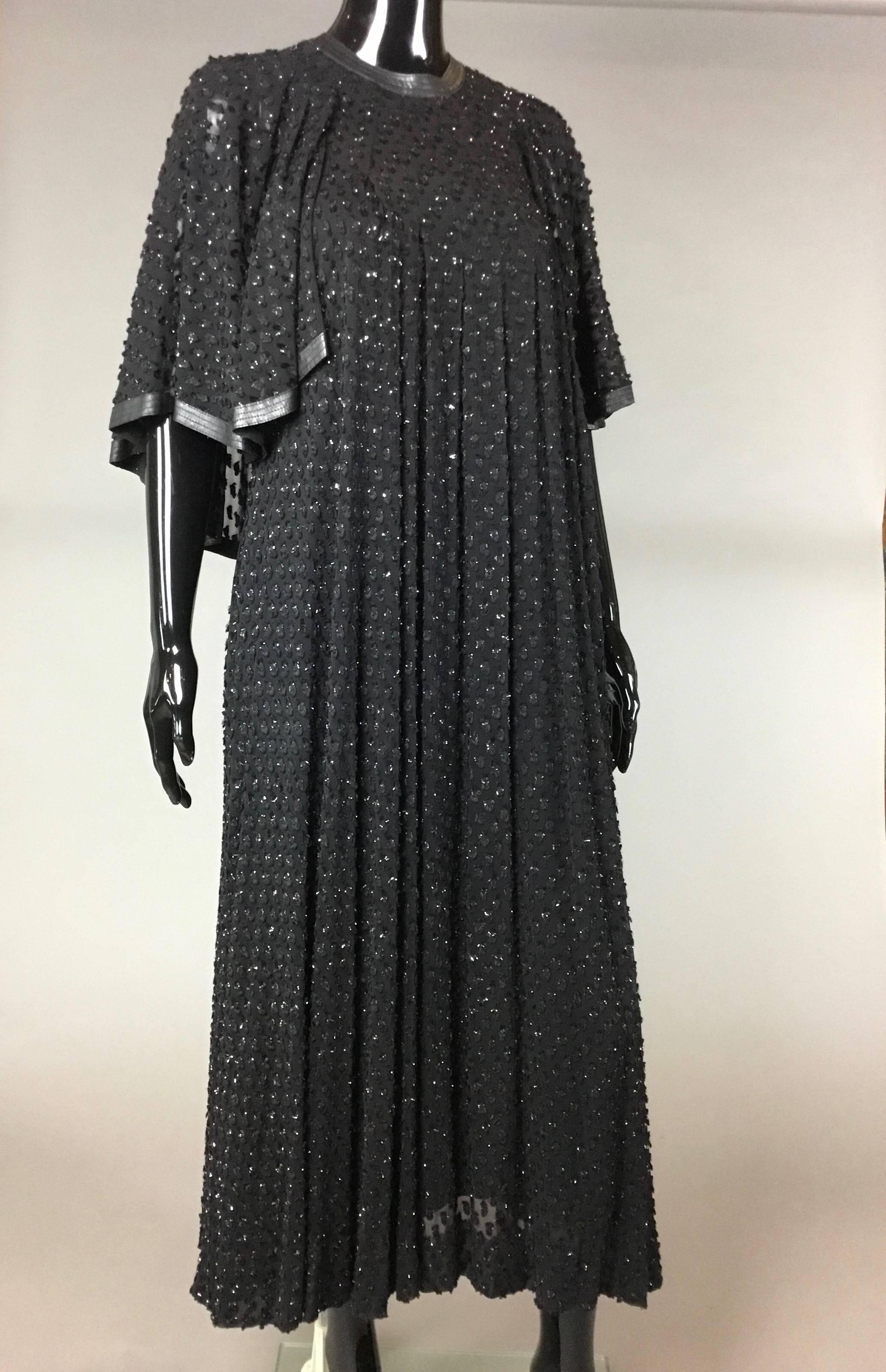 A beautiful long Jean Muir devoré dress. The fabric has raised velvet with just a hint of sparkle. it is high necked with a fine band of leather as trim. A thirties style integral cape looks like sleeves at front and drapes lower at back, with the