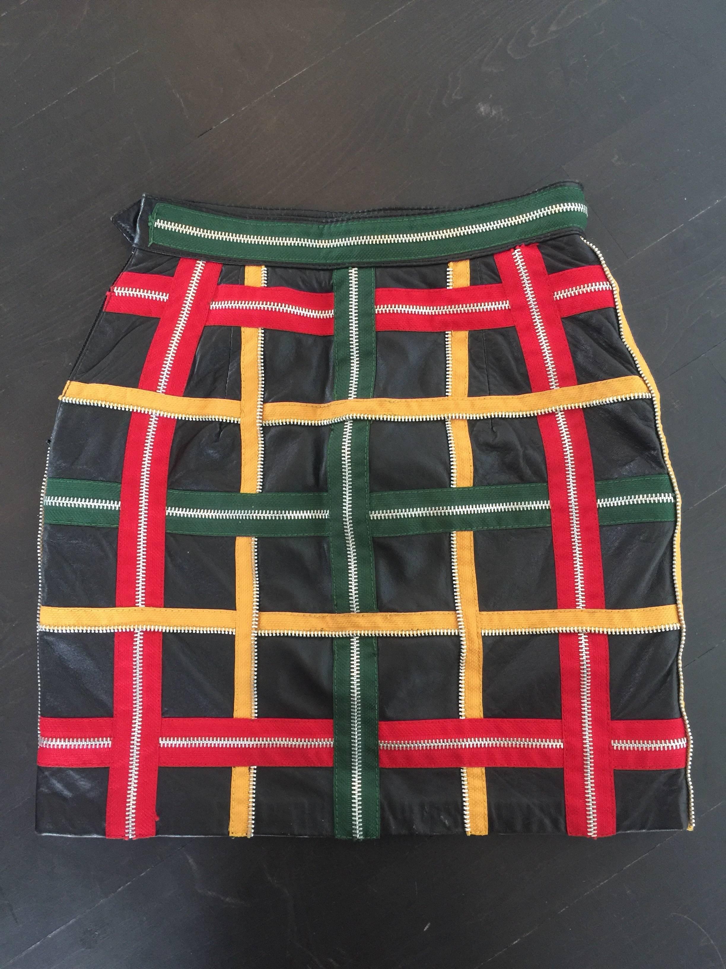 This mini skirt by Moschino is from the late 80's or early 90's. It is made of black leather with an overlay of red, green and yellow zippers. The zipper details have silver hardware and criss cross to form a plaid pattern. The skirt is fully lined