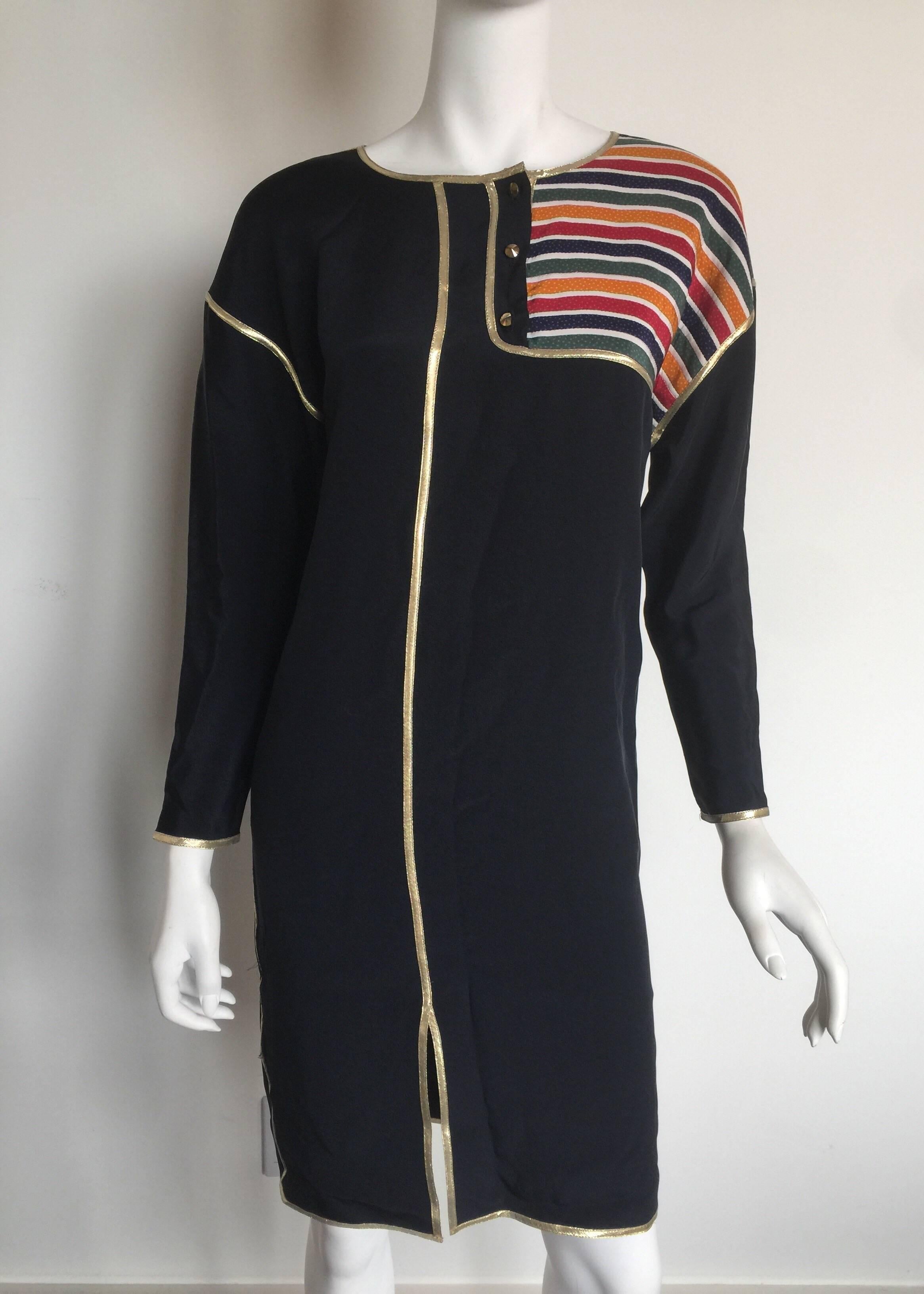 This 1980's asymmetrical stripe dress by Geoffrey Beene combines the comfort of a roomy shift silhouette with flashy gold trim and multi-colored stripes. It offers a mid-thigh slit on the right leg and three gold buttons at the collar. This navy