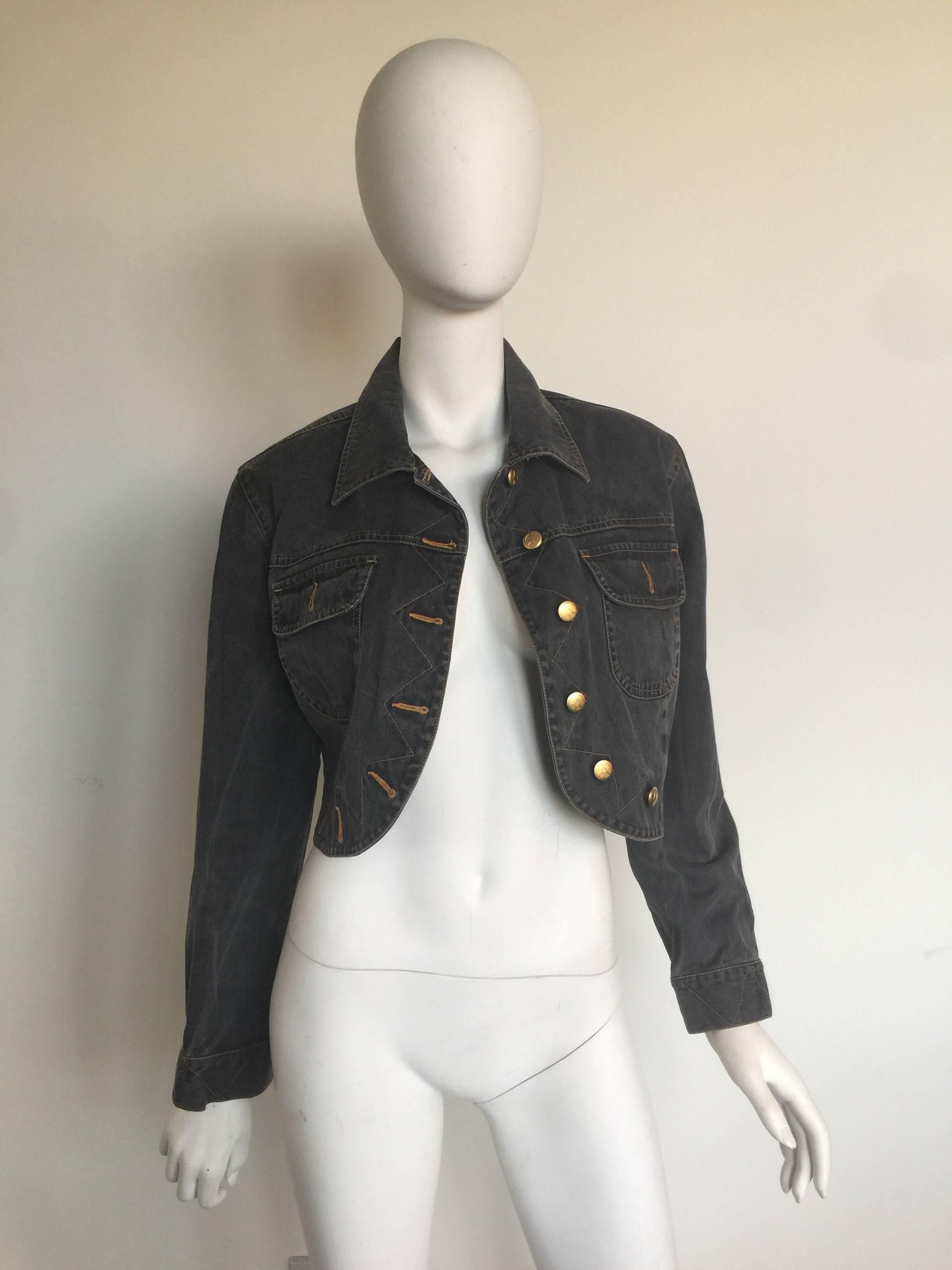 This cropped denim jacket has gold peace sign buttons and pocket details.  It is from the 1980s.  It is a dark grey blue in color.  It has two front pockets and all buttons in good condition. 