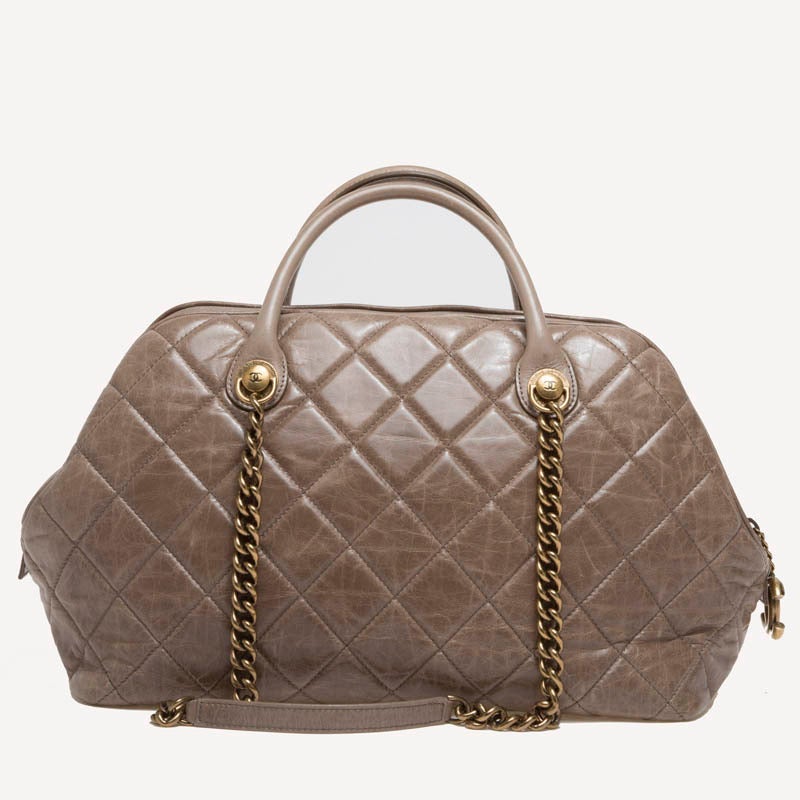 This authentic Chanel Castle Rock Bowler in Large is constructed with stunning diamond quilting on aged calfskin leather. This bag features dual-rolled handles, double-brass chain link straps and top zipper closure with CC chain. The aged gold-tone