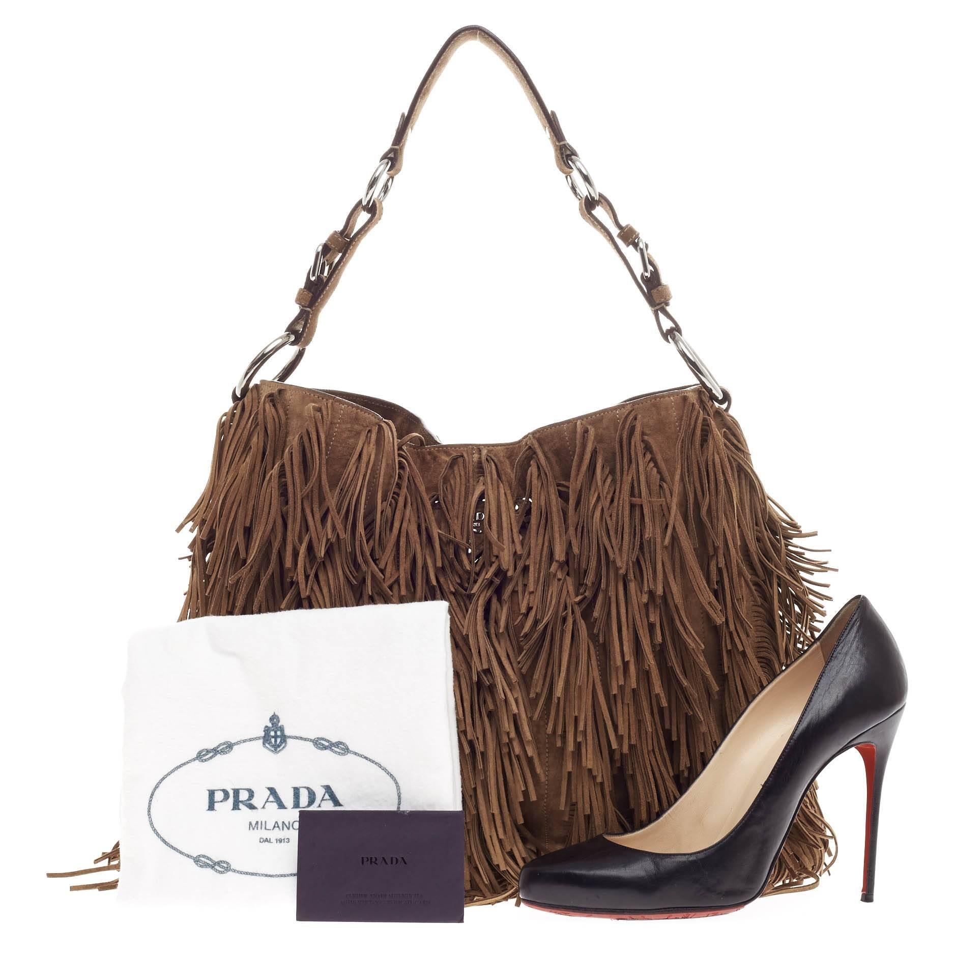 This authentic Prada Fringe Hobo Suede Medium is showcases Prada's unique and eye-catching fashion forward style. Constructed in brown suede, this 70's inspired hobo features all-over cascading long fringe details, a single belted strap with