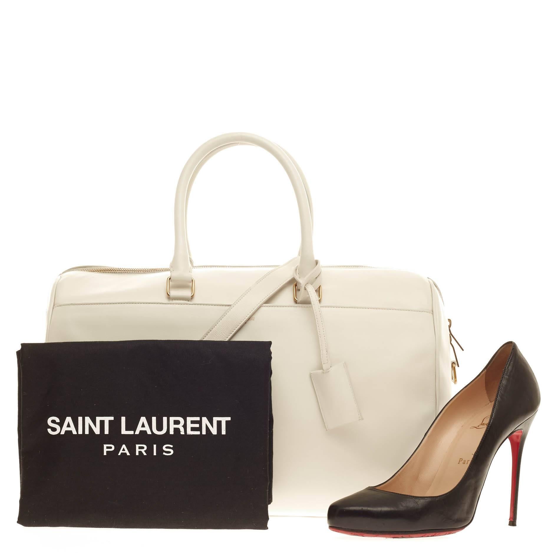 This authentic Saint Laurent Classic Duffle Leather 12 is a sleek, modern and an elegant duffle bag to travel in style with. Crafted in traditional white leather and gold-tone hardware accents, this alluring bag can be carried conveniently