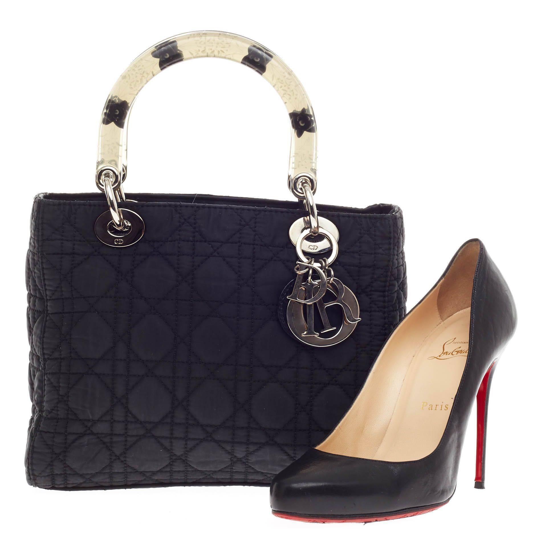 This authentic Christian Dior Lady Dior Cannage Quilt Nylon Medium is a no-fuss, elegant piece that every fashionista needs in her wardrobe. Crafted from black cannage quilted nylon, this boxy bag features short dual clear handles with flower print