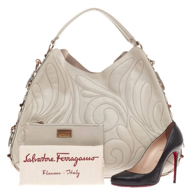 This authentic Salvatore Ferragamo Fergie Hobo Embroidered Leather showcases a sophisticated  contemporary design. Crafted from cream leather, this luxurious flat hobo features embroidered petals on leather, all-around belted metal clips design,