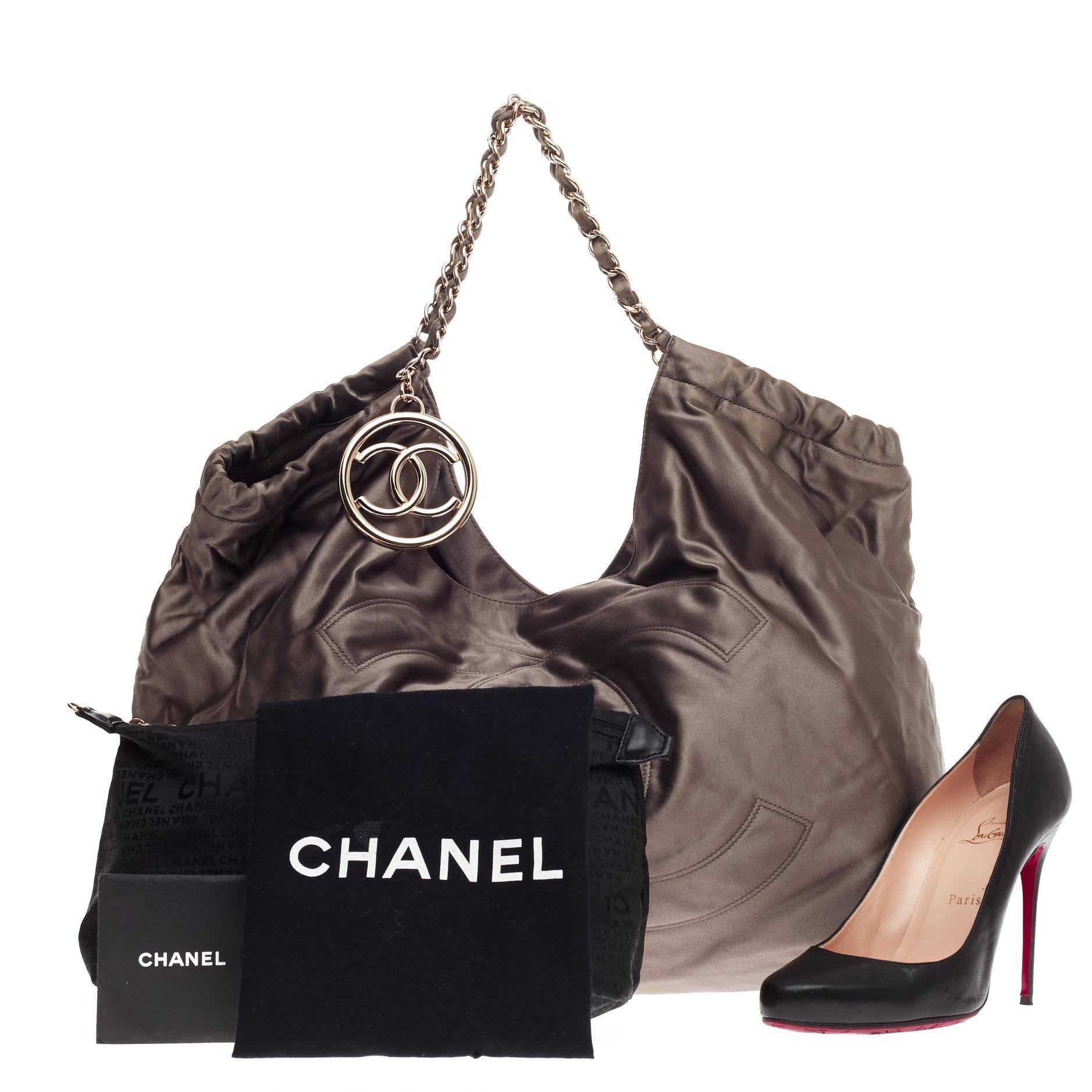 This authentic Chanel Coco Cabas Satin Large is perfect for your casual wear. Crafted from gray satin, this roomy hobo features an oversized stitched Chanel CC frontal logo, ruching detail, CC silver charm, woven-in satin chain strap, and