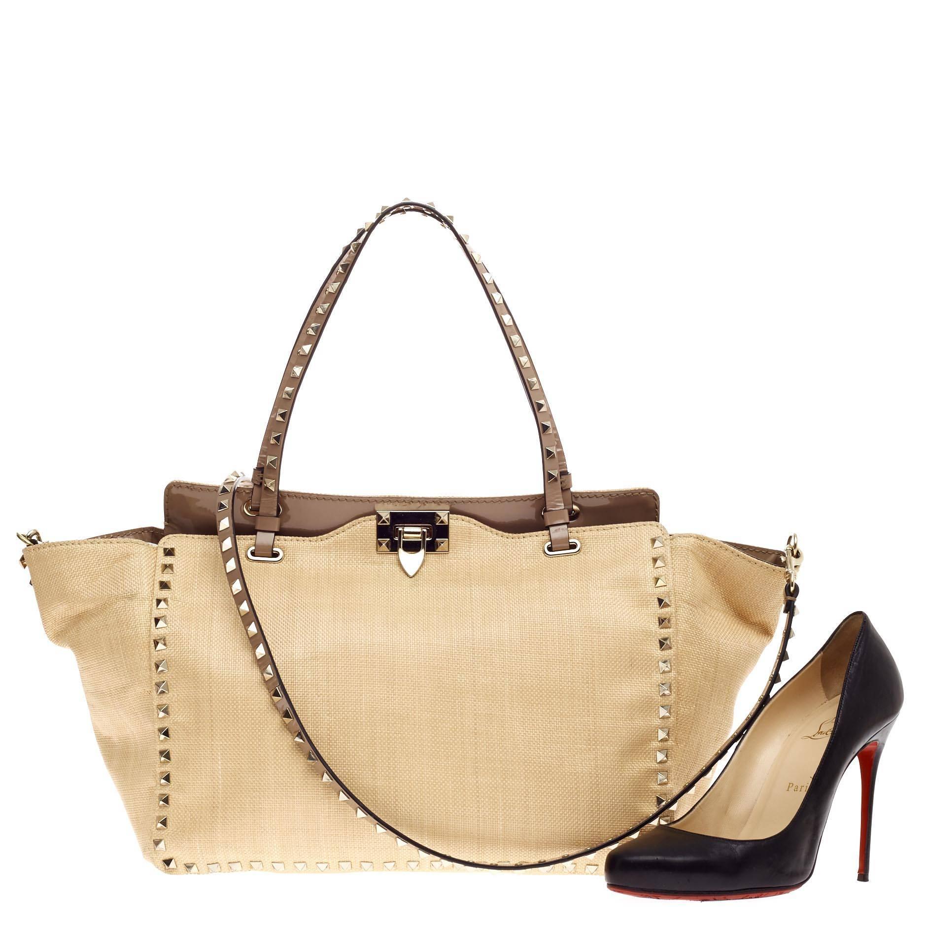 This authentic Valentino Rockstud Tote Raffia Medium is the perfect daily bag for the on-the-go fashionista. Crafted from beautiful, durable raffia with patent leather trims, this tote features dual flat studded patent leather handles, gold-tone