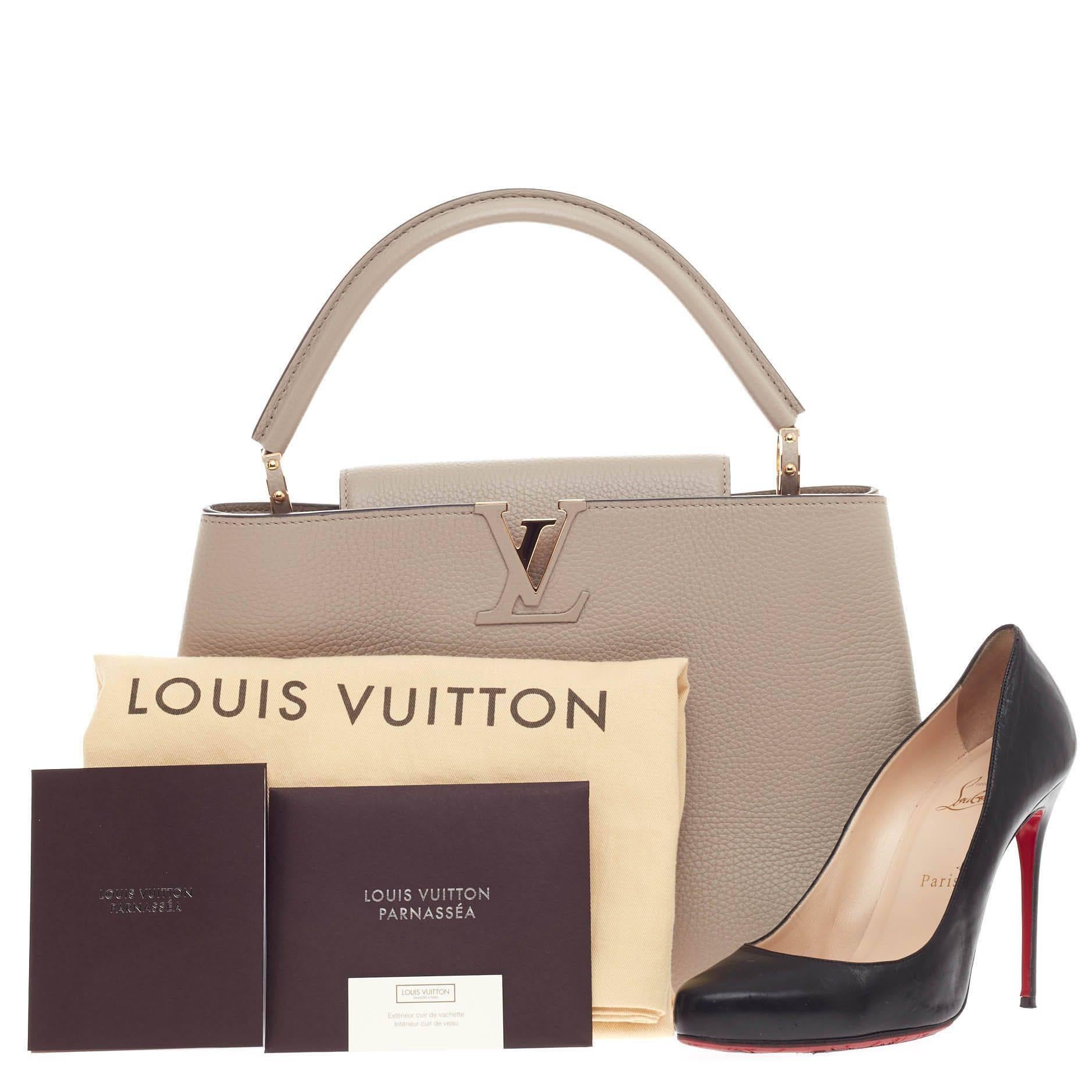 This authentic Louis Vuitton Capucines Leather MM is sophisticated and ladylike luxurious bag from the brand's Fall 2013 Collection inspired by its Parisian heritage. Crafted in galet beige taurillion leather, this chic, stand-out bag features a