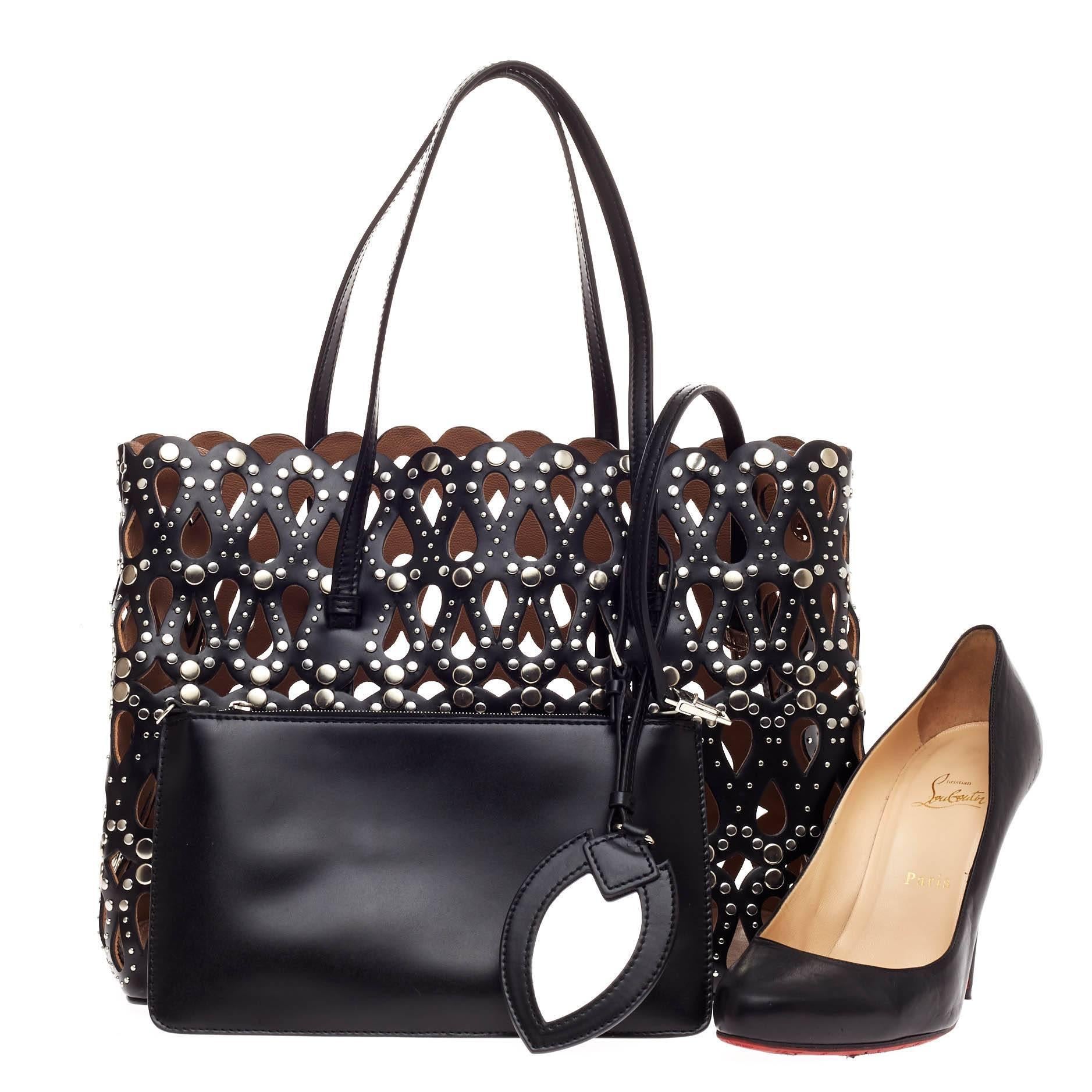 This authentic Alaia Studded Open Tote Laser Cut Leather Medium is your perfect everyday bag. Crafted from black laser cut leather exterior, this edgy, cult-favorite tote features multiple silver studs embellishments, protective base studs, and