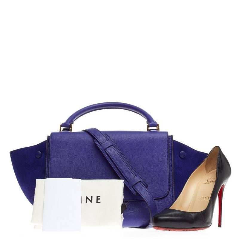 This authentic Celine Trapeze Grainy Leather Mini is a modern minimalist design with a playful twist. Crafted from indigo royal blue leather with matching suede wings. this classic tote features rolled top handle, exterior back pocket, expanded side