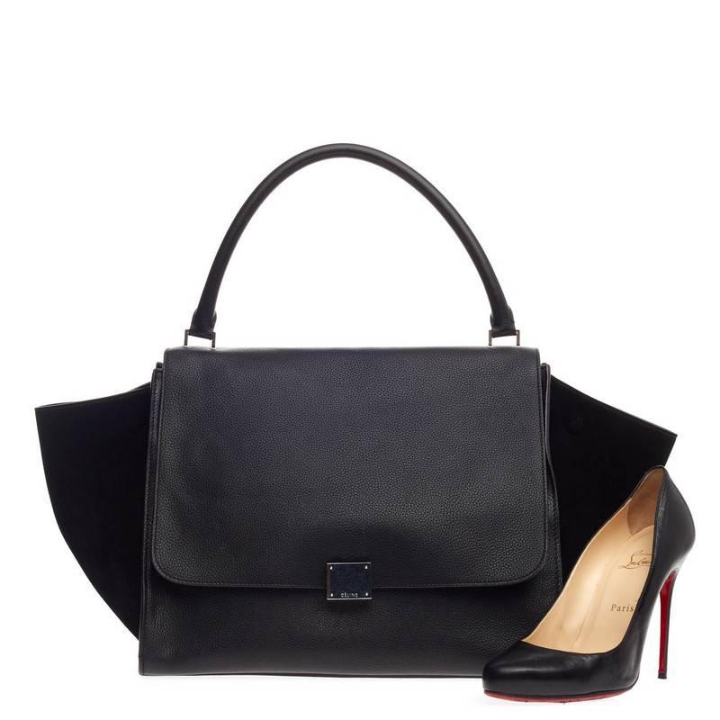 This authentic Celine Trapeze Leather Large is a modern minimalist design with a playful twist in subdued colors. Crafted from black leather and suede wings, this classic tote features a top rolled handle, side snap closures, exterior back pocket,