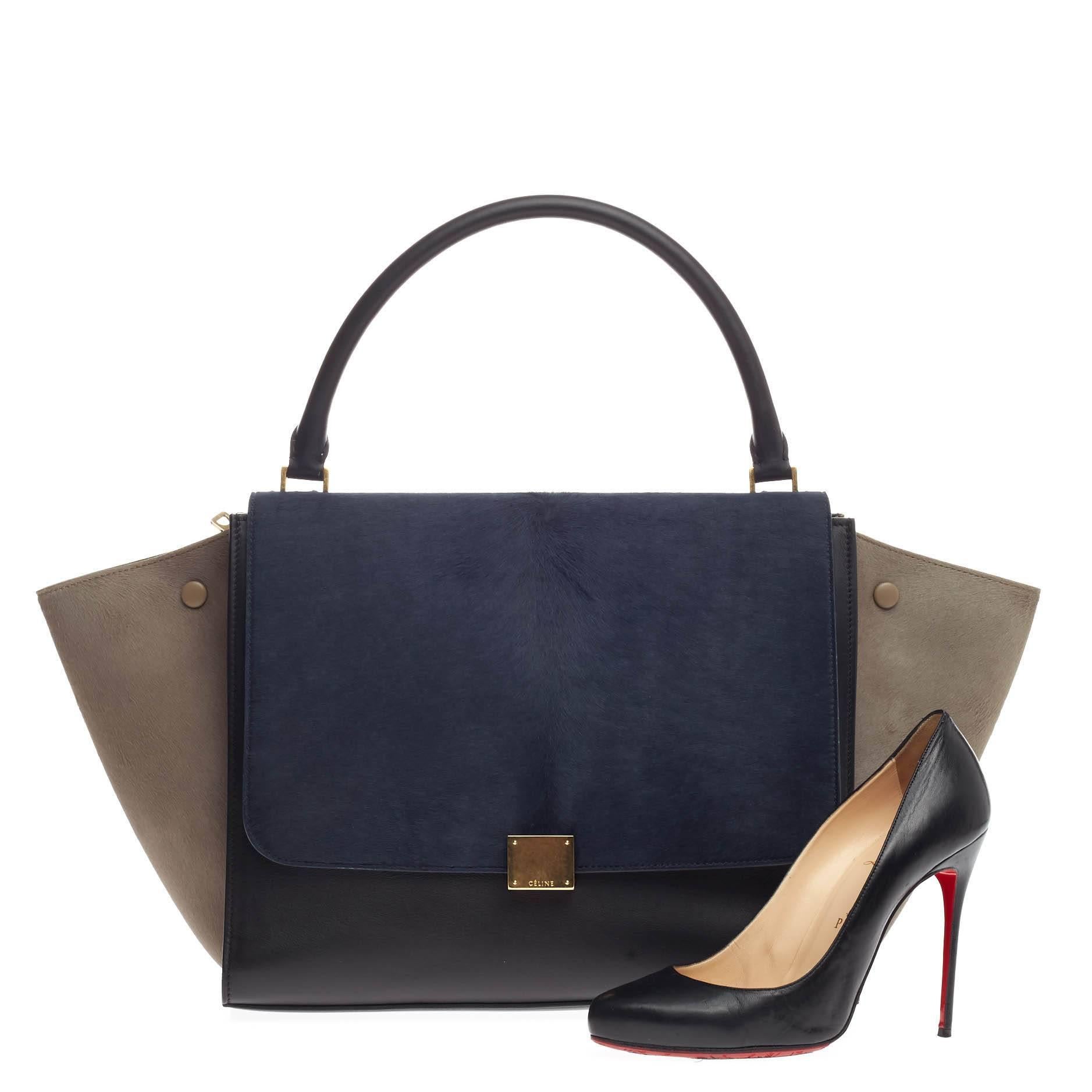 This authentic Celine Tricolor Trapeze Pony Hair Large is a modern minimalist design with a playful twist in an array of subdued colors. Crafted from tricolor navy blue, taupe pony hair and black leather, this classic tote features a top looped