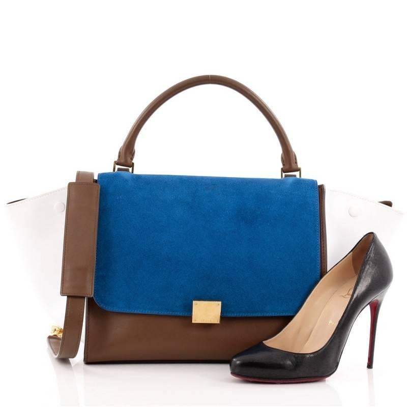 This authentic Celine Tricolor Trapeze Suede Medium is a modern minimalist design with a playful twist in an array of subdued colors. Crafted from brown leather and blue suede flap with white leather side wings, this classic tote features rolled top