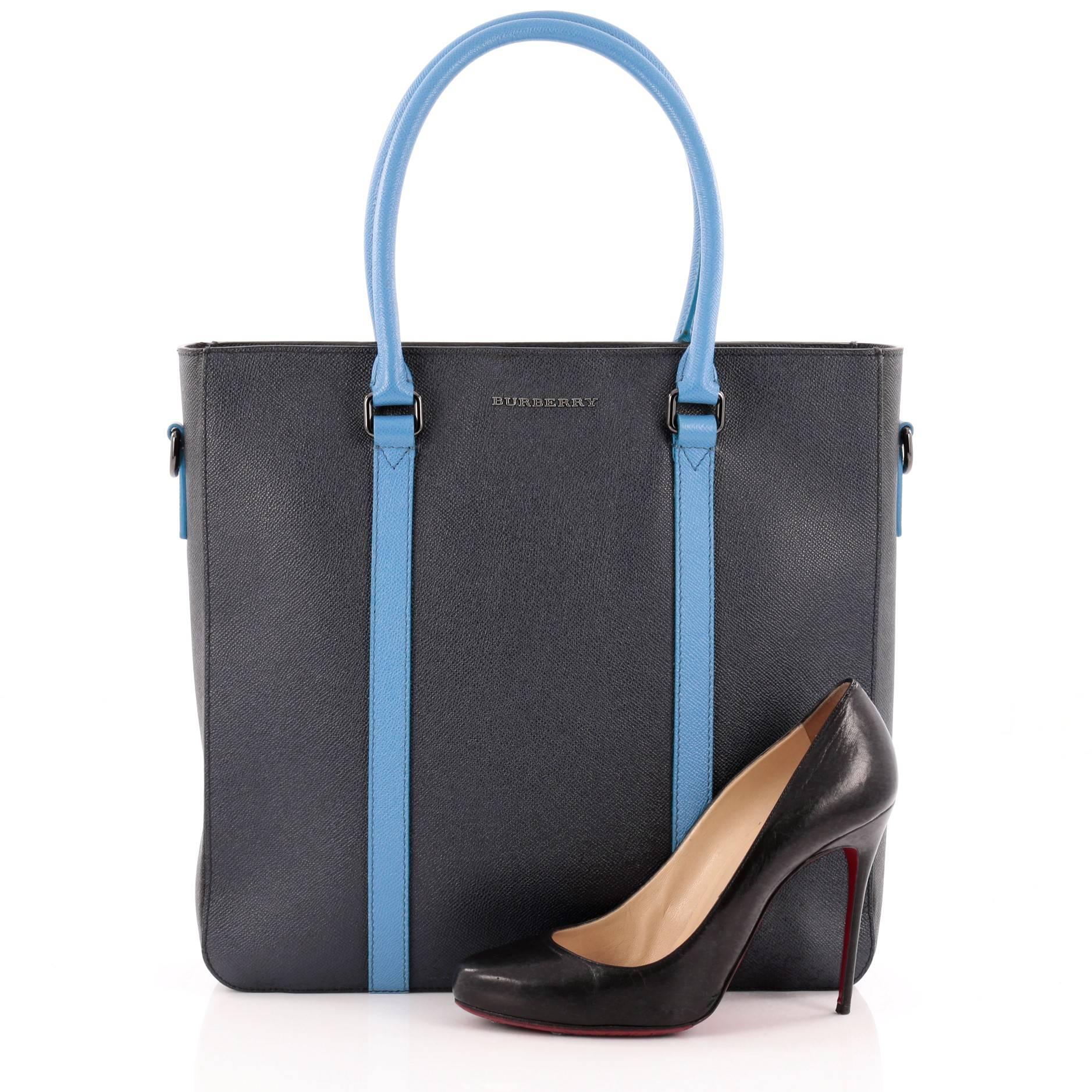This authentic Burberry Kenneth Tote Saffiano Leather Medium displays a structured and clean urban style. Crafted from navy blue textured leather with sky blue leather trims, this chic tote features dual-rolled top handles, logo lettering at front
