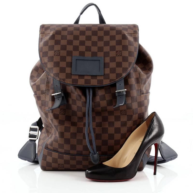This authentic Louis Vuitton Runner Backpack Damier displays a sleek modern shape of a backpack that looks truly elegant. Crafted from damier ebene coated canvas with dark blue leather trims, this bag features rolled leather top handle, two