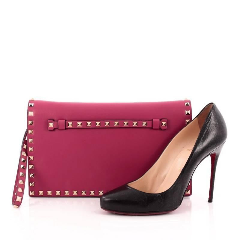 This authentic Valentino Rockstud Flap Clutch Leather is a chic yet functional accessory perfect for on-the-go moments. Crafted from raspberry smooth leather, this trendy clutch features a leather hand sling, back hand strap, polished gold Valentino
