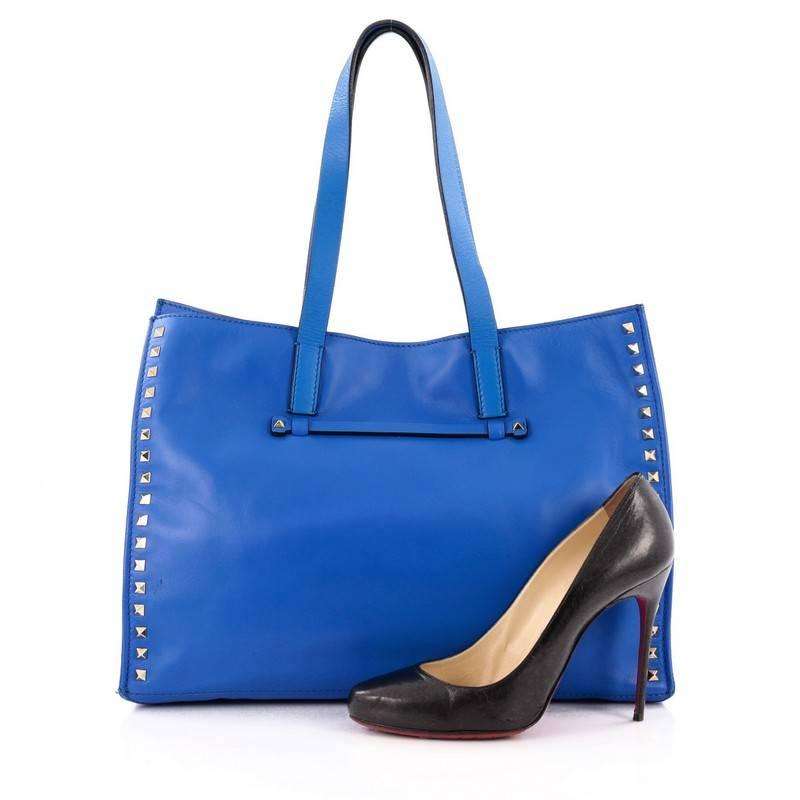 This authentic Valentino Rockstud Open Tote Leather Medium is a stylishly edgy bag that is one of today's most sought-after styles. Crafted from royal blue smooth leather, this eye-catching tote features dual flat tall leather handles, signature