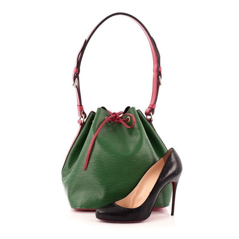 This authentic Louis Vuitton Petit Noe Handbag Epi Leather is a chic and iconic bag that is timeless. Crafted from borneo green epi leather with contrast rouge red leather and trims, this bucket bag features an adjustable red leather shoulder strap,