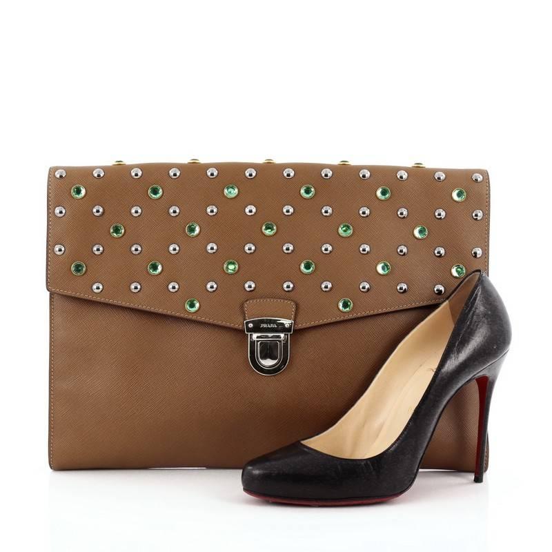 This authentic Prada Push Lock Portfolio Handbag Studded Saffiano Leather Large is a chic in design perfect for office use or night outs. Crafted from brown saffiano leather, this oversized, flat clutch features embellished studs and green crystals,