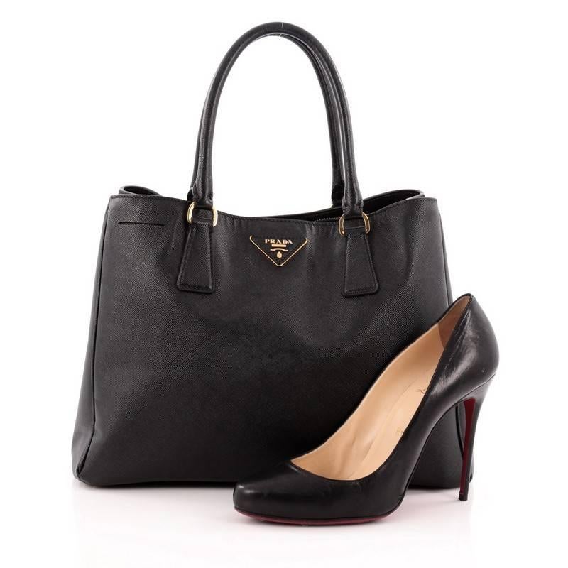 This authentic Prada Gardener's Tote Saffiano Leather Medium is the perfect bag to complete any outfit. Crafted from black saffiano leather, this boxy tote features side snap buttons, raised Prada logo, dual-rolled leather handles protective base
