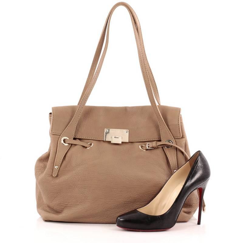 This authentic Jimmy Choo Rhys Tote Leather from the brand's 2011 Collection adds a refined touch to everyday looks. Crafted from light brown leather, this soft-structured tote features dual slim handles, belted drawstring top, flap with flip-lock
