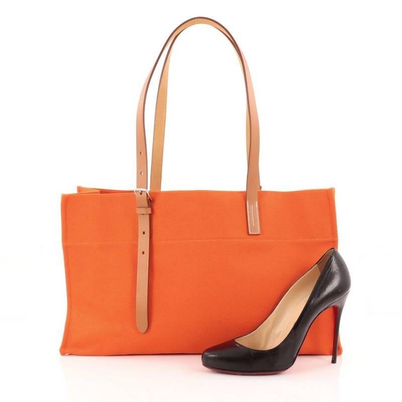 This authentic Hermes Etriviere Elan Shopping Tote Toile and Leather is lightweight and casual perfect for everyday use. Crafted from orange fabric with natural vache hunter leather trims, this tote features dual-flat adjustable leather handles,