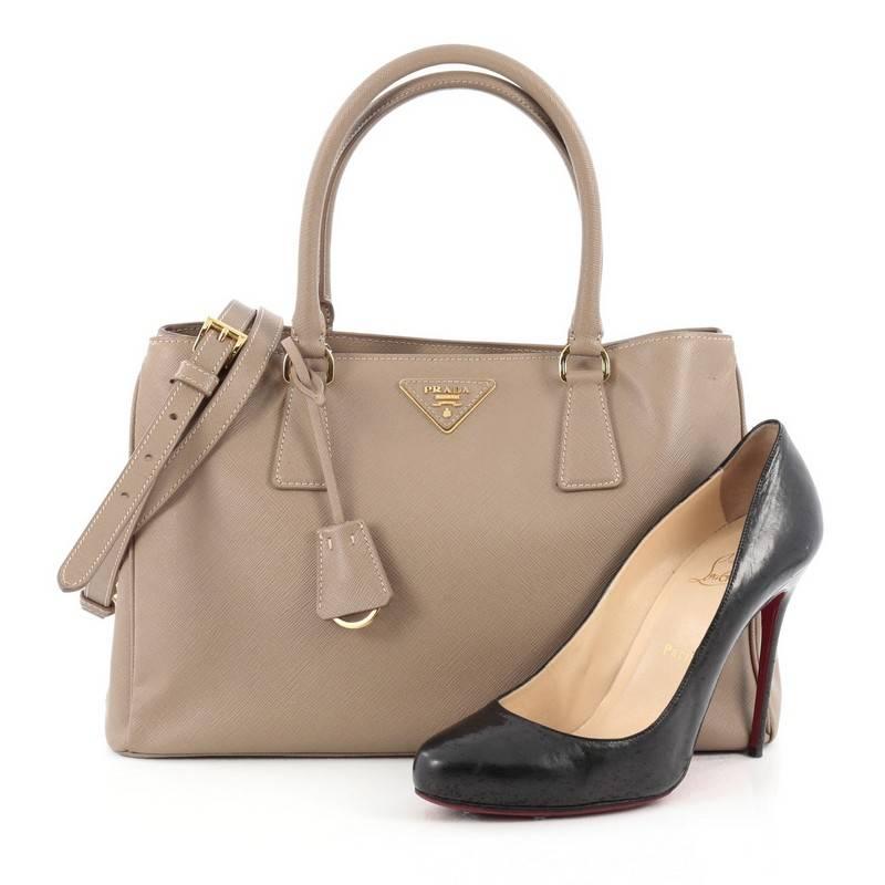 This authentic Prada Gardener's Tote Saffiano Leather Medium is elegant in its simplicity and structure. Crafted from beige saffiano leather, this tote features dual-rolled leather handles, raised Prada logo, protective base studs, and gold-tone