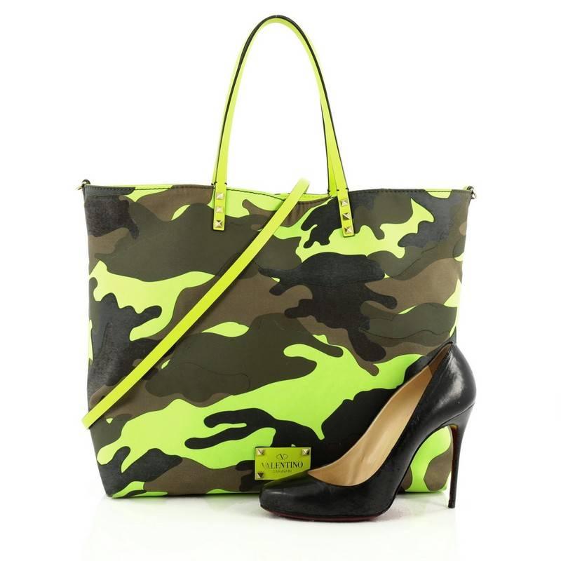 This authentic Valentino Rockstud Open Reversible Convertible Tote Camo Canvas Large is the perfect daily bag for an on-the-go fashionista. Crafted in canvas with neon green and camo on its reversible side, this chic, stand-out tote features the