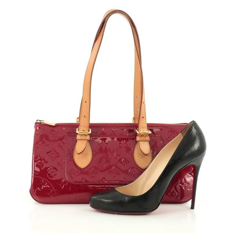 This authentic Louis Vuitton Rosewood Avenue Handbag Monogram Vernis is a striking, fun accessory to carry with its unique triangular silhouette. Crafted from red monogram vernis leather, this no-fuss bag is accented with dual-rolled vachetta