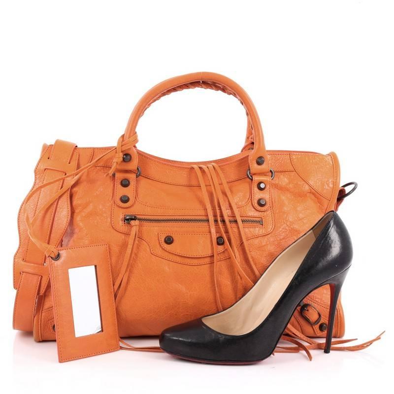 This authentic Balenciaga City Classic Studs Handbag Leather Medium is for the on-the-go fashionista. Constructed in tangerine orange leather, this popular bag features dual braided woven handle straps, front zip pocket, iconic Balenciaga classic