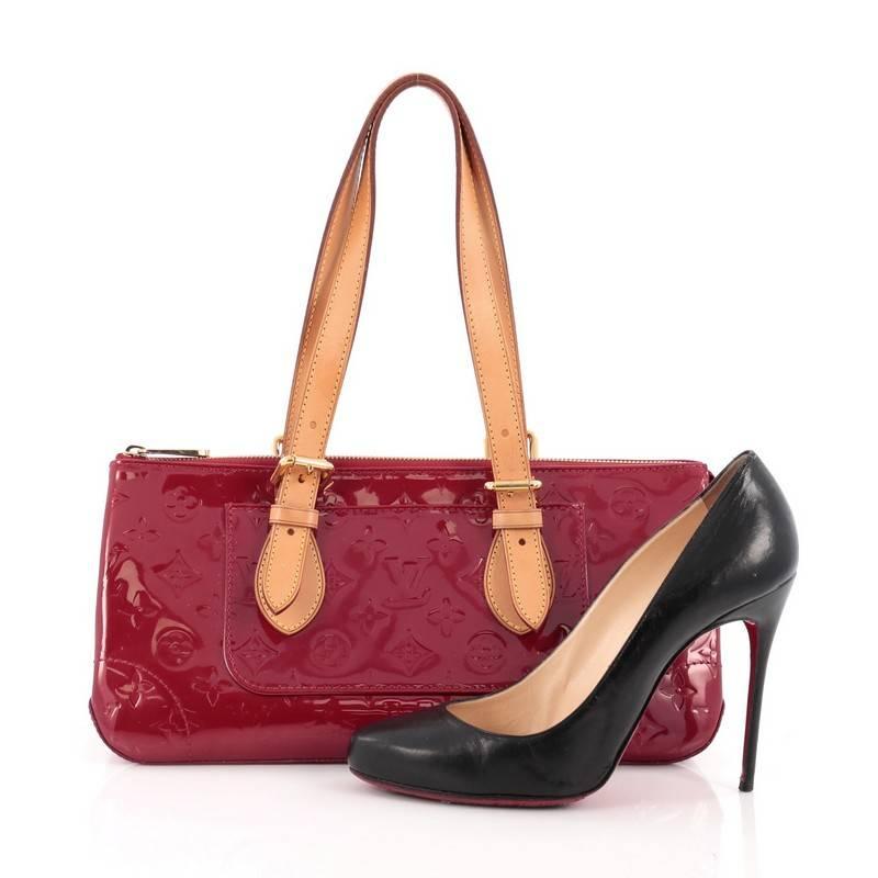 This authentic Louis Vuitton Rosewood Avenue Handbag Monogram Vernis is a striking, fun accessory to carry with its unique triangular silhouette. Crafted from pomme d'amour red monogram vernis, this no-fuss bag is accented with dual-flat vachetta