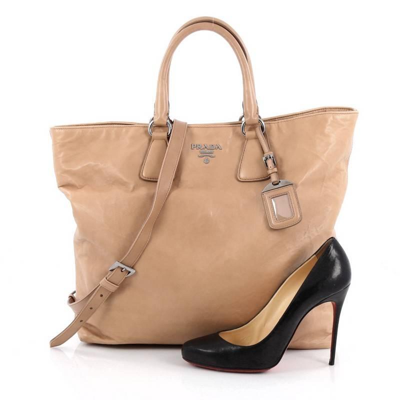 This authentic Prada Convertible Shopper Tote Soft Calfskin Large exudes a stylish and industrial design made for everyday excursions. Crafted from nude soft calfskin leather, this tote features dual-rolled leather handles, raised gold Prada Milano