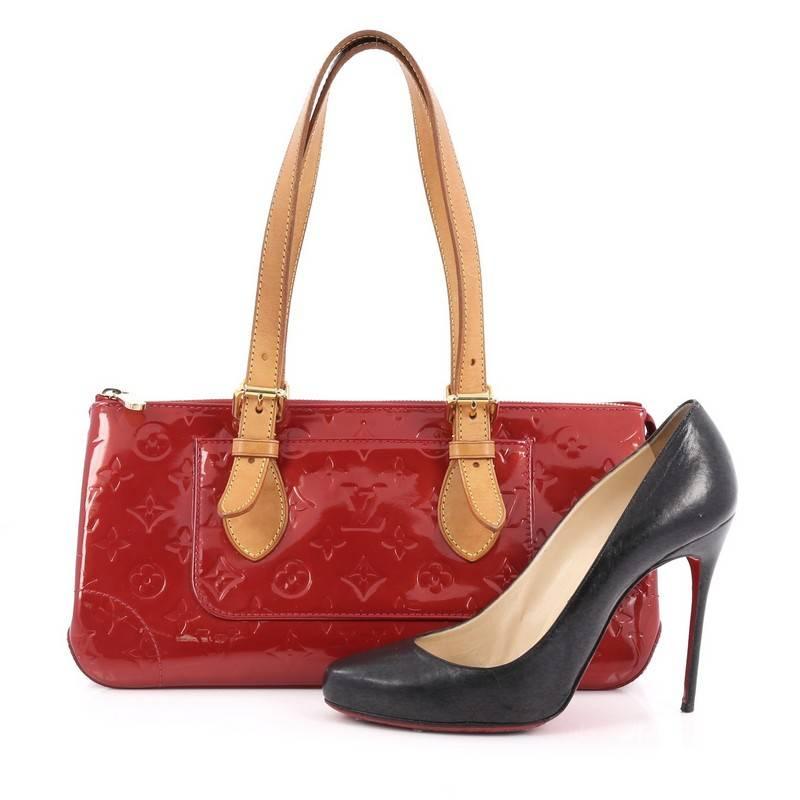 This authentic Louis Vuitton Rosewood Avenue Handbag Monogram Vernis is a striking, fun accessory to carry with its unique triangular silhouette. Crafted from pomme d'amore red monogram vernis, this no-fuss bag is accented with dual-rolled vachetta
